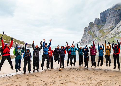 Trip participants jump in unison on a beach in Lofoten, Norway.