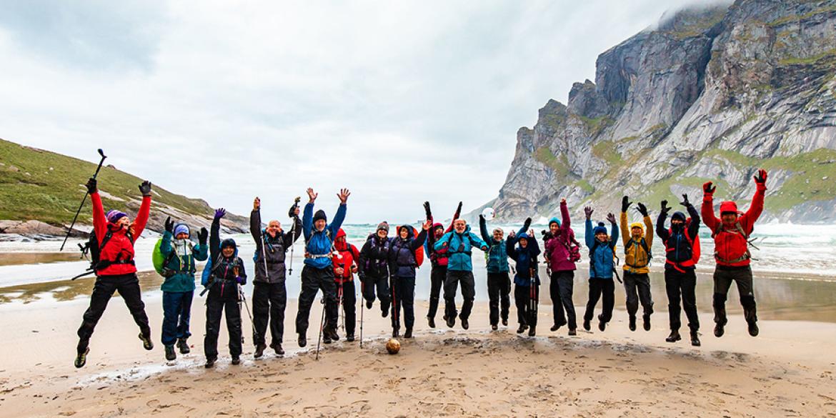 Trip participants jump in unison on a beach in Lofoten Islands, Norway