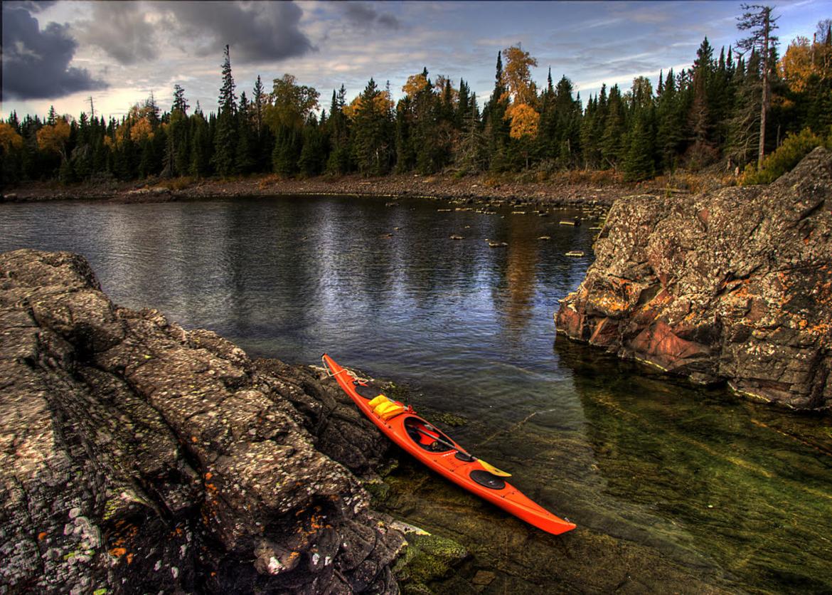 A kayak beached on a rock. It sits beside a body of water bordered by forest.