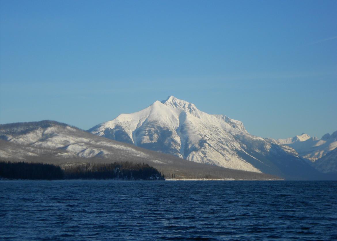 A snowy mountain seen from the opposite side of a body of water.
