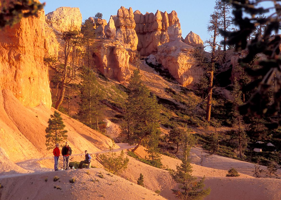 Three people stand on a trail in front of a canyon.