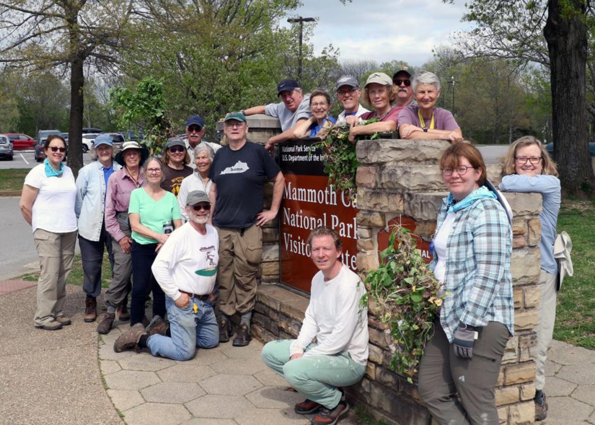 Eighteen smiling participants pose around a sign reading "Mammoth Cave National Park Visitor Center."