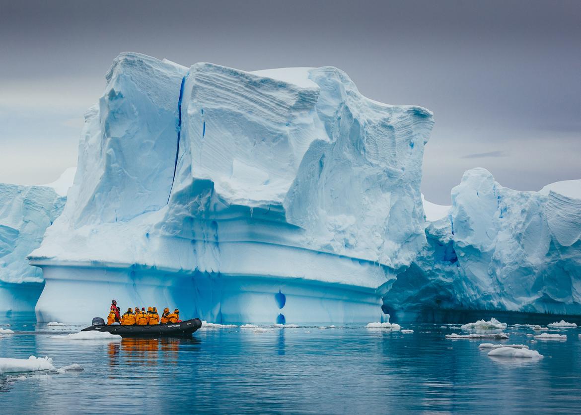 A raft full of participants in front of a vibrant blue iceberg