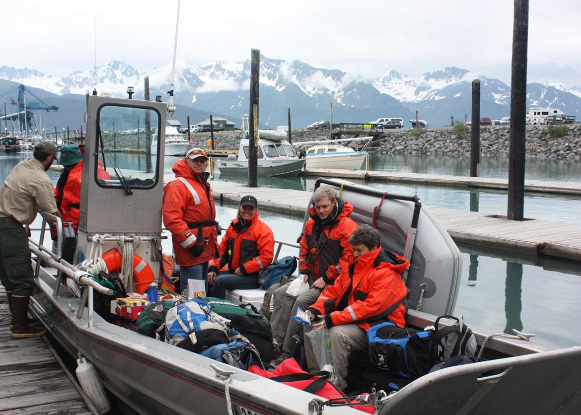 Trip participants wearing bright orange jackets sitting on a boat in Resurrection Bay, Alaska with snow-covered mountains in backgorund
