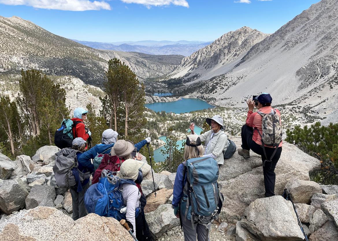 Group of trip participants hiking in Eastern Sierras, California, surrounded by rocky mountain vistas and a teal-blue lake.