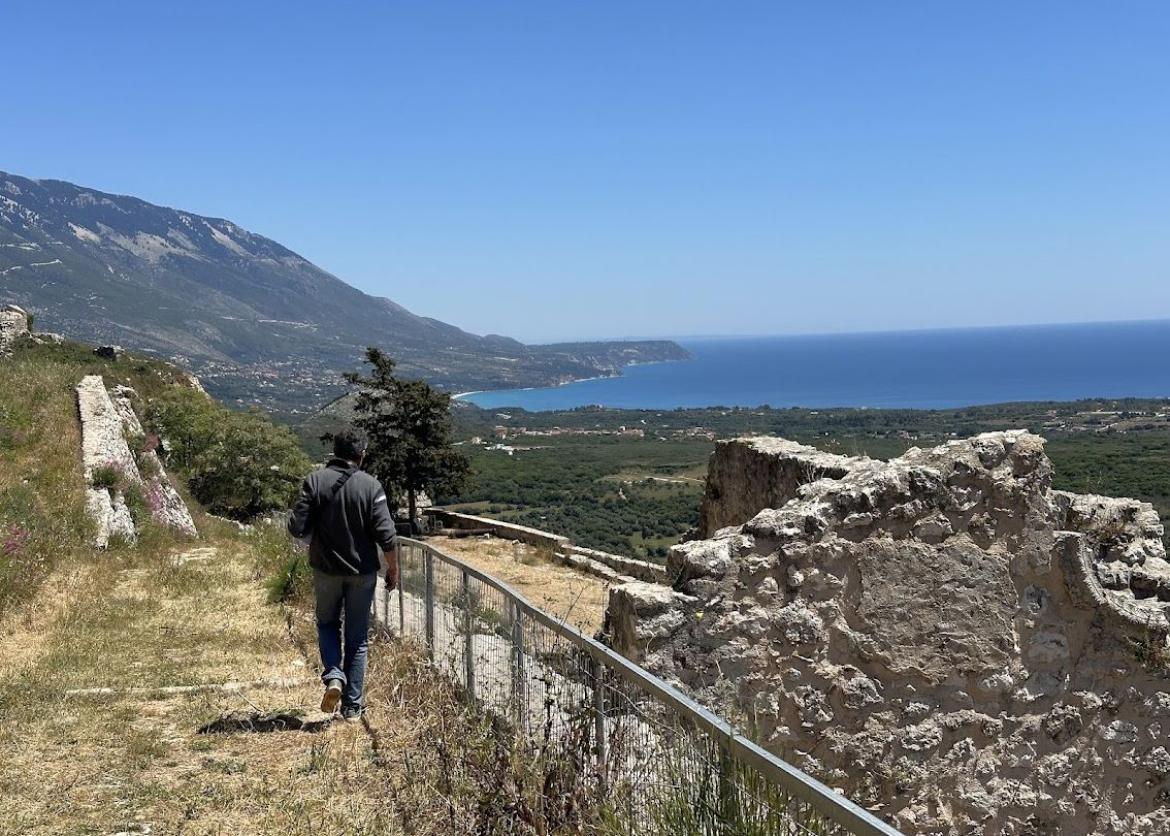 Man hikes on a trail overlooking a mountainside and the Ionian Sea.