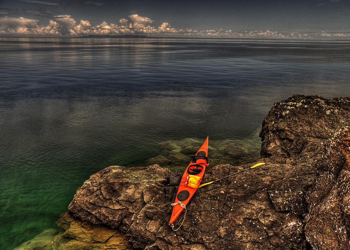 A kayak rests on a rock next to calm water. The water stretches to the horizon.