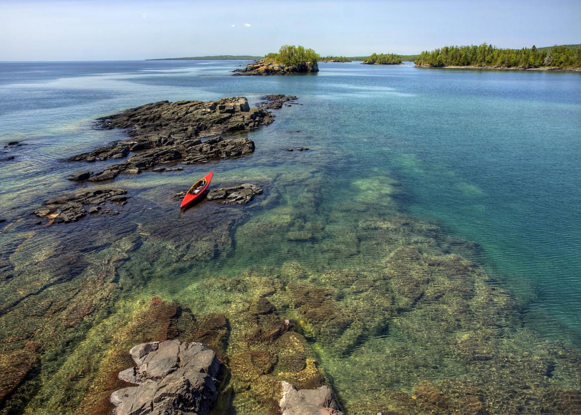 A kayak rests on a rock. A series of rocks break the surface of the water.