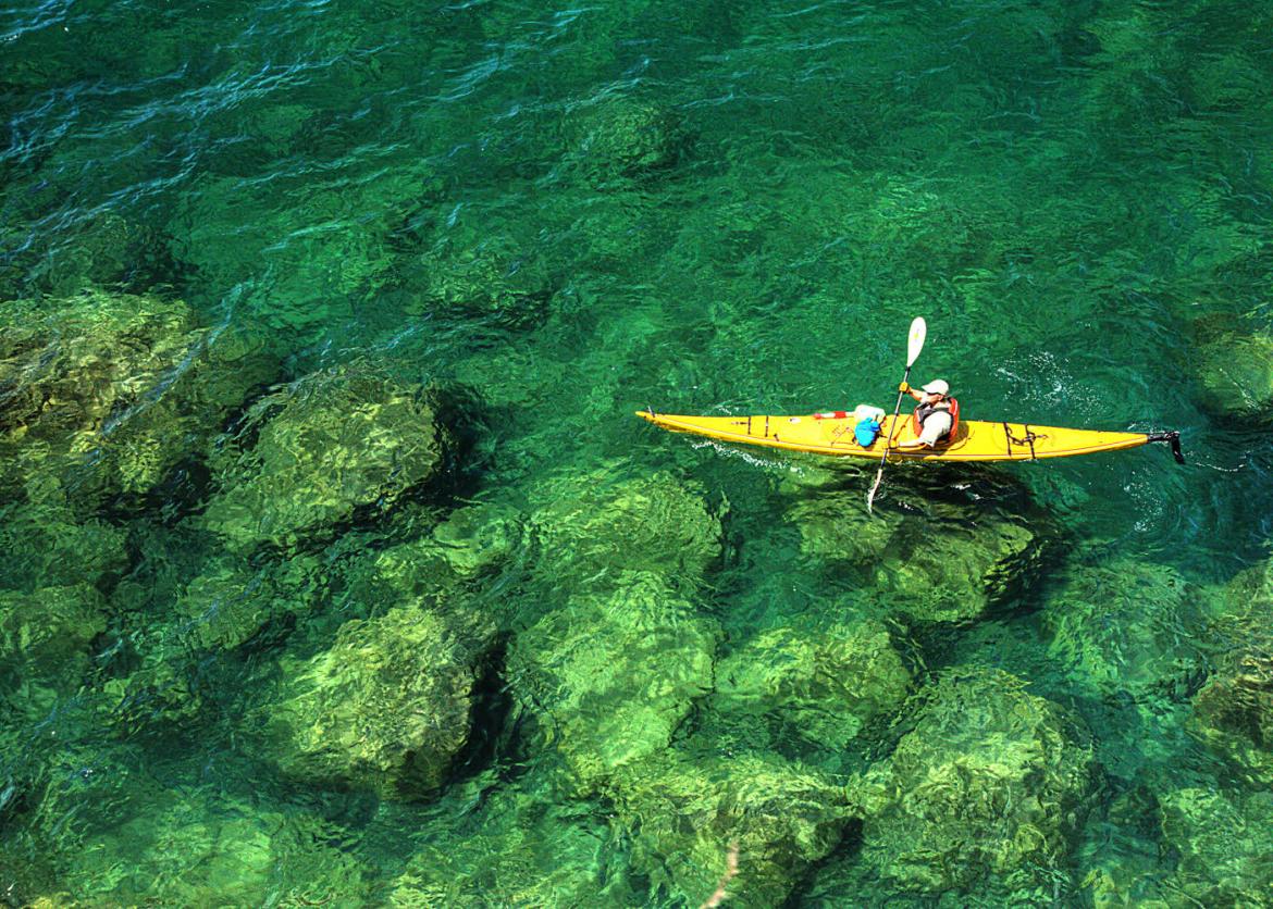 A kayaker seen from above paddling through clear green water.