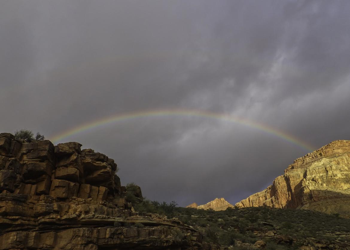 A rainbow appearing between two canyons in the gloomy sky.