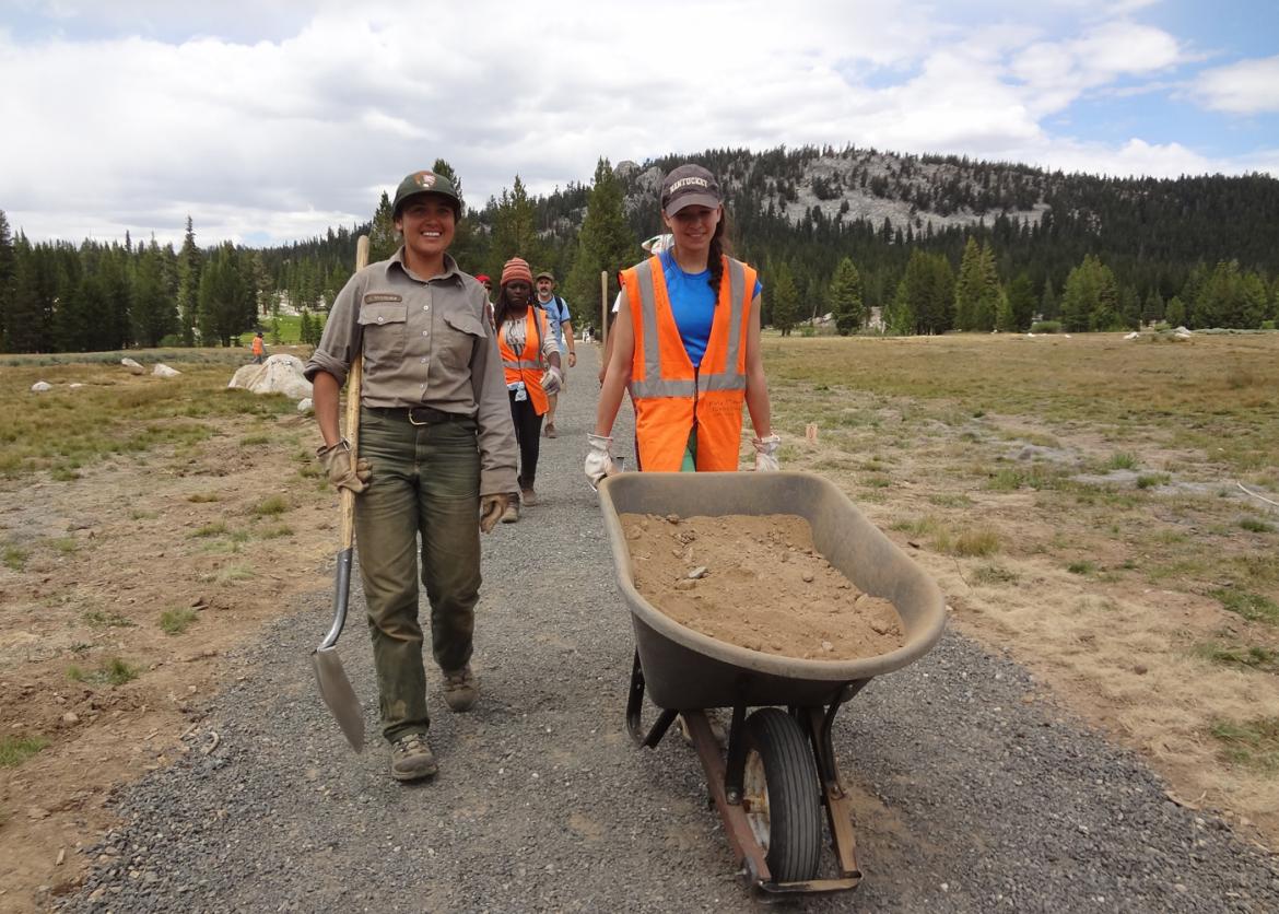 Participants and park service rangers walking on trail with a wheel barrow