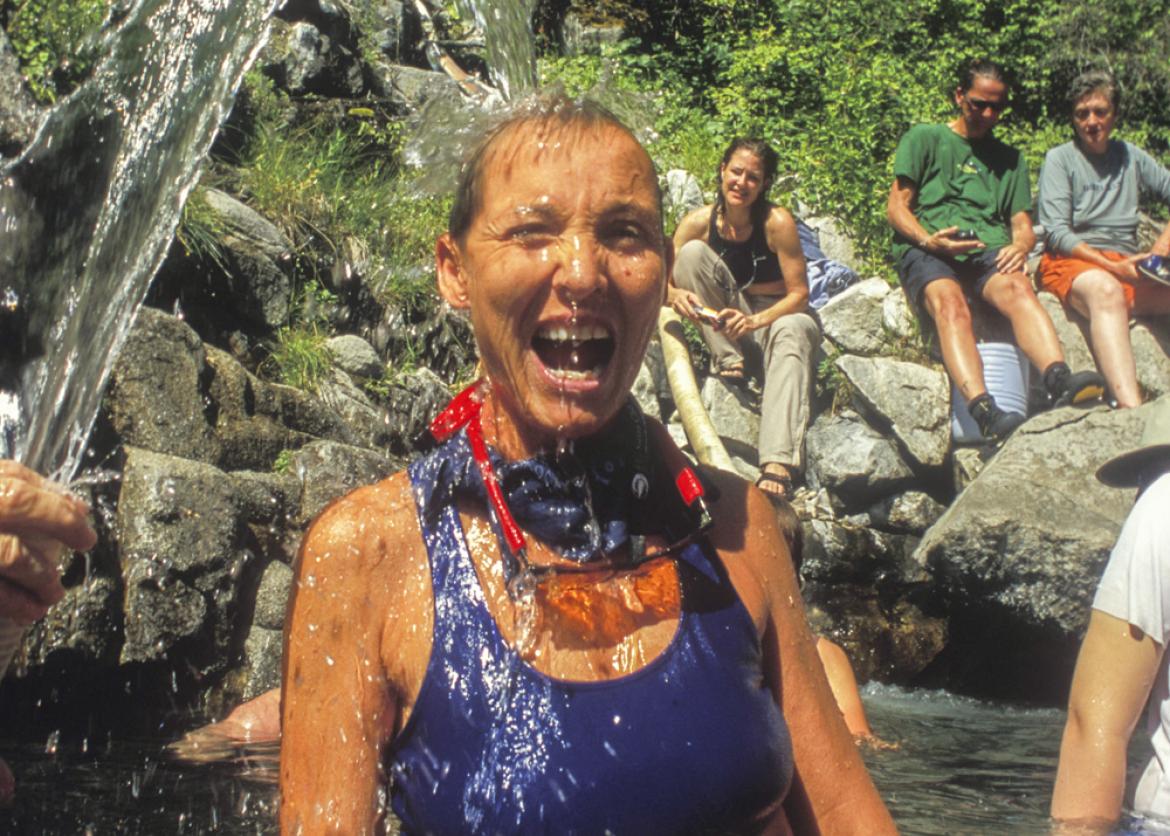 A woman with her mouth open gets sprayed by a stream of water as she stands submerged to her waist.