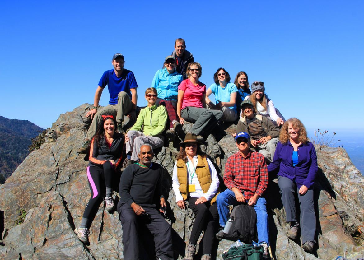 A group sitting on a big rock with the clear sky in the bbackground, happily posing for the photo