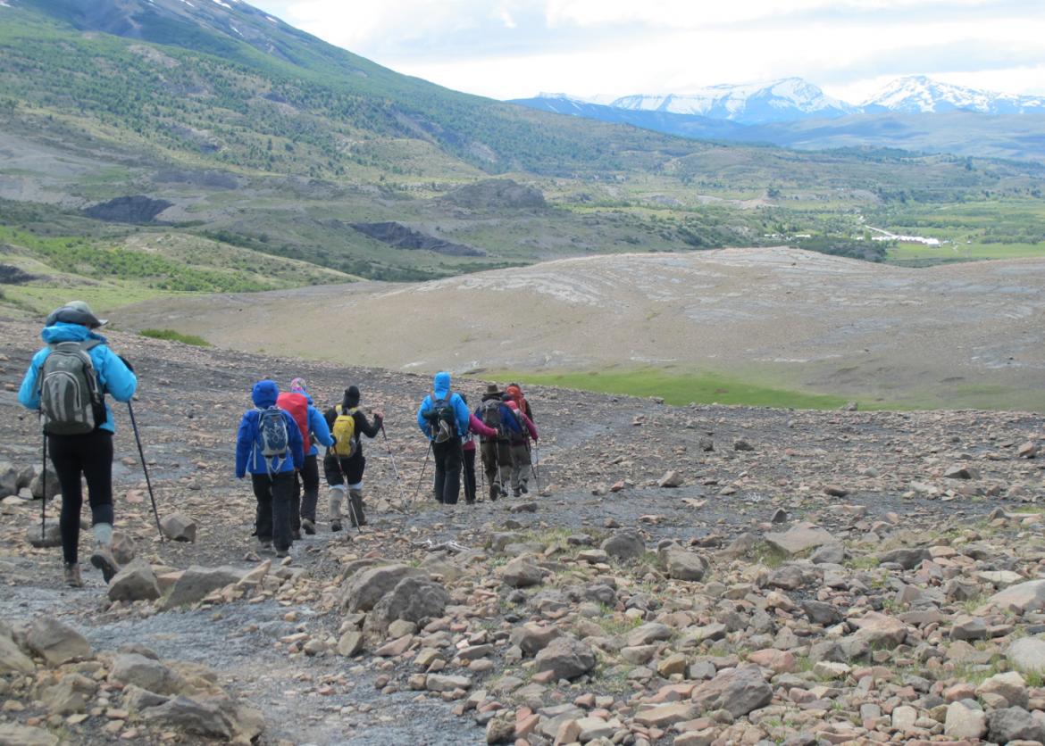 Hikers trek single file across rocky ground.