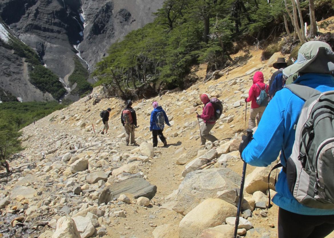 Seven hikers trek downhill on a rocky slope.