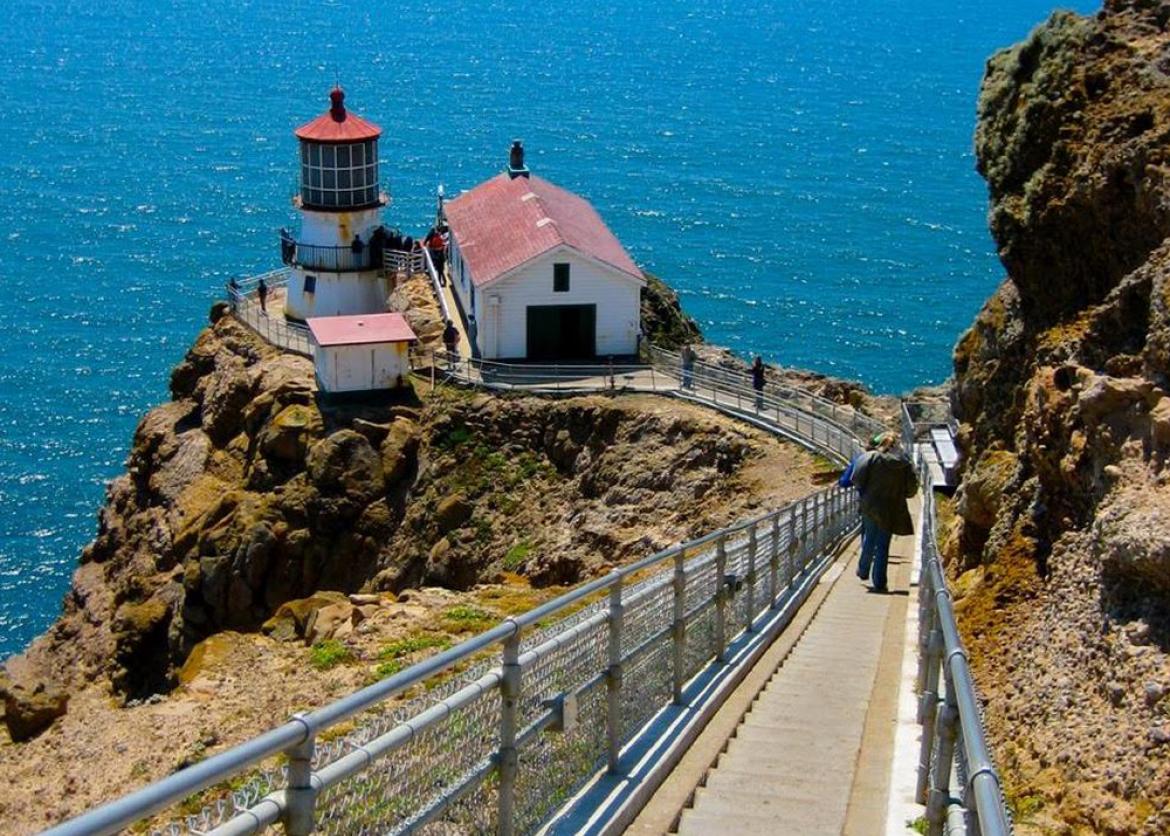 A person walking down the stairs to the lighthouse with a view of the water.