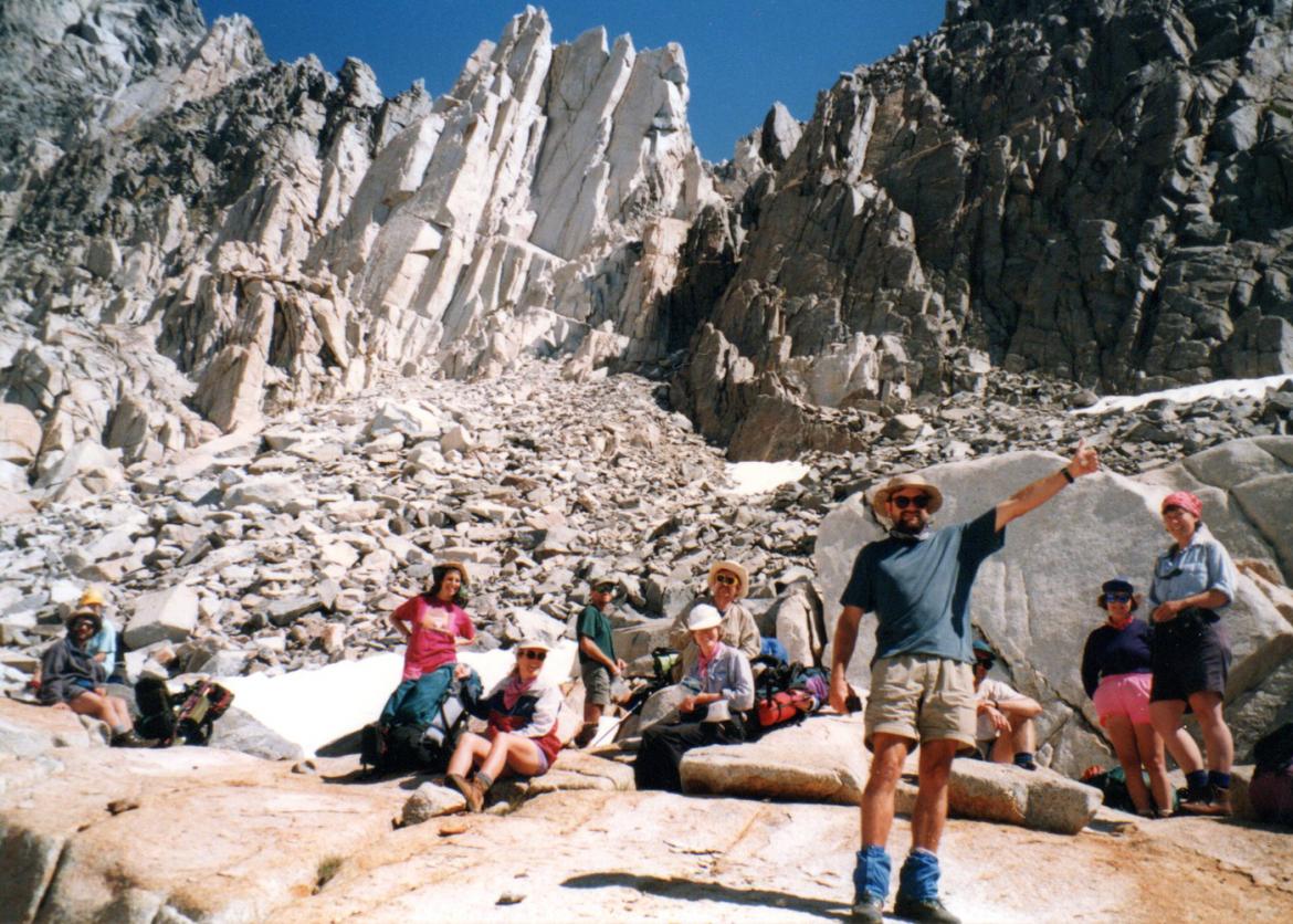 A group taking a break as one man waves and points up to the sky.