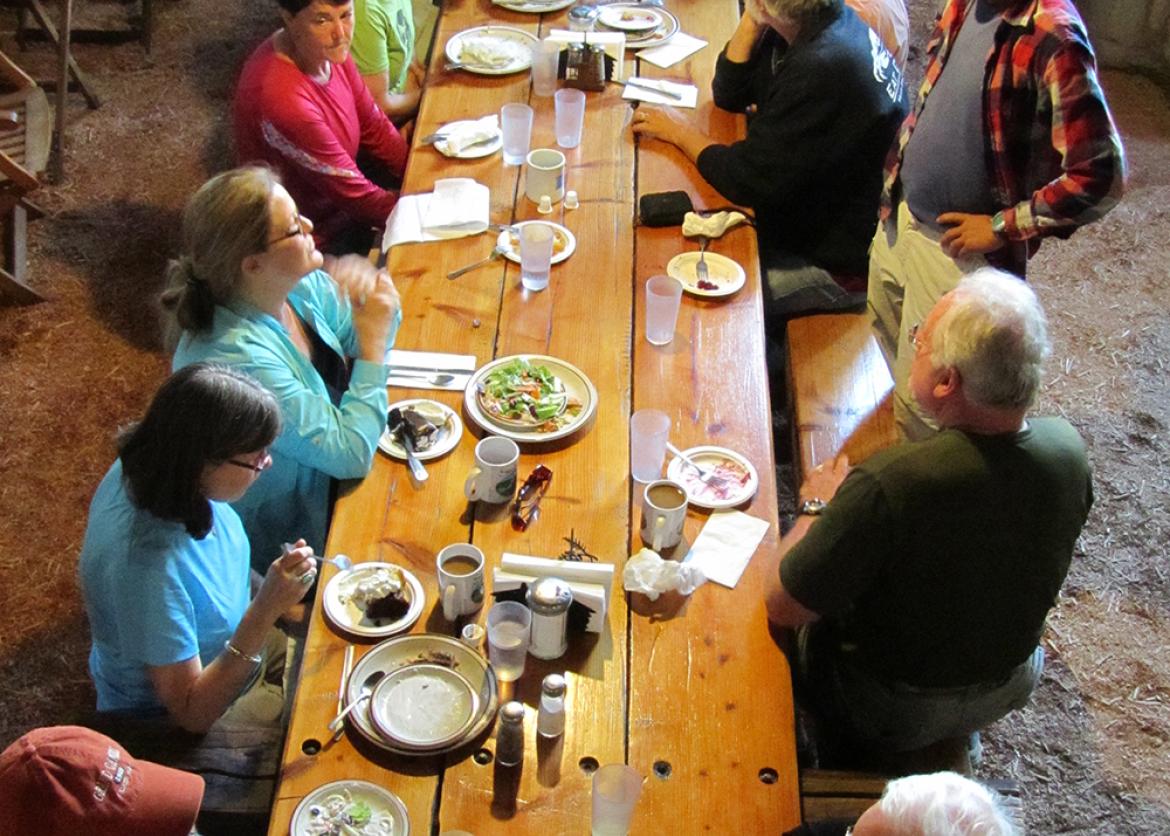 Fifteen people eating together at a long wooden table.