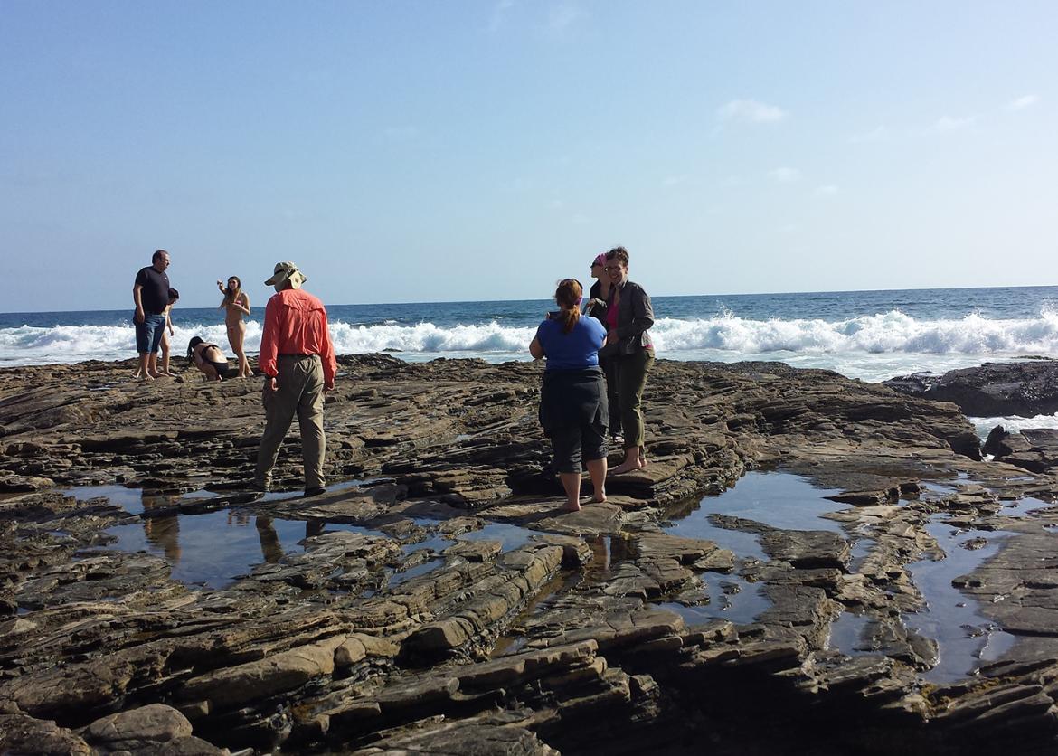 A group of people stopping on the side rocks to admire the view of the ocean.