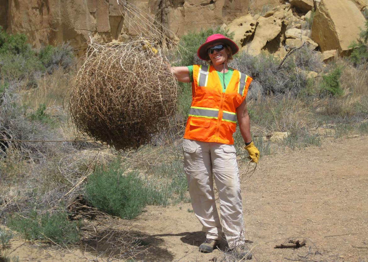 A woman smiling as she holds up a round haystack.