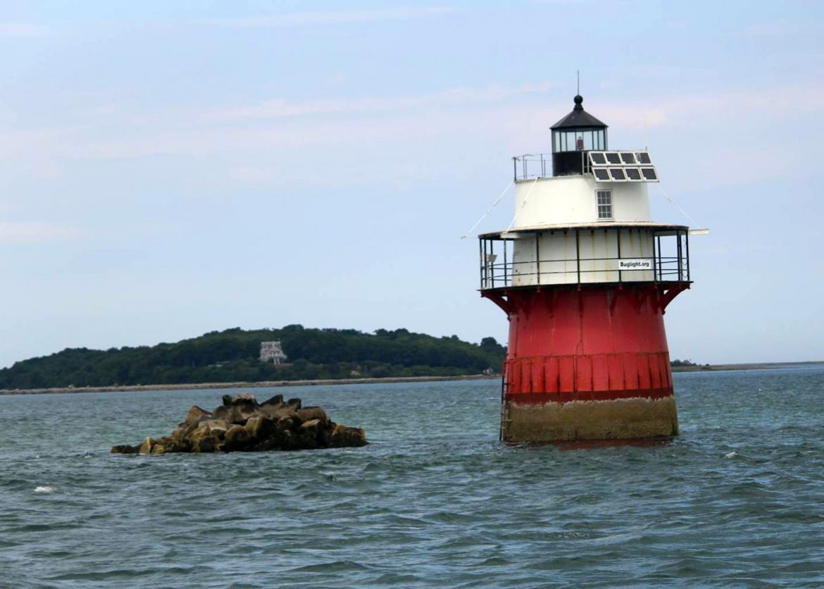 A red and light lighthouse in the middle of the water.
