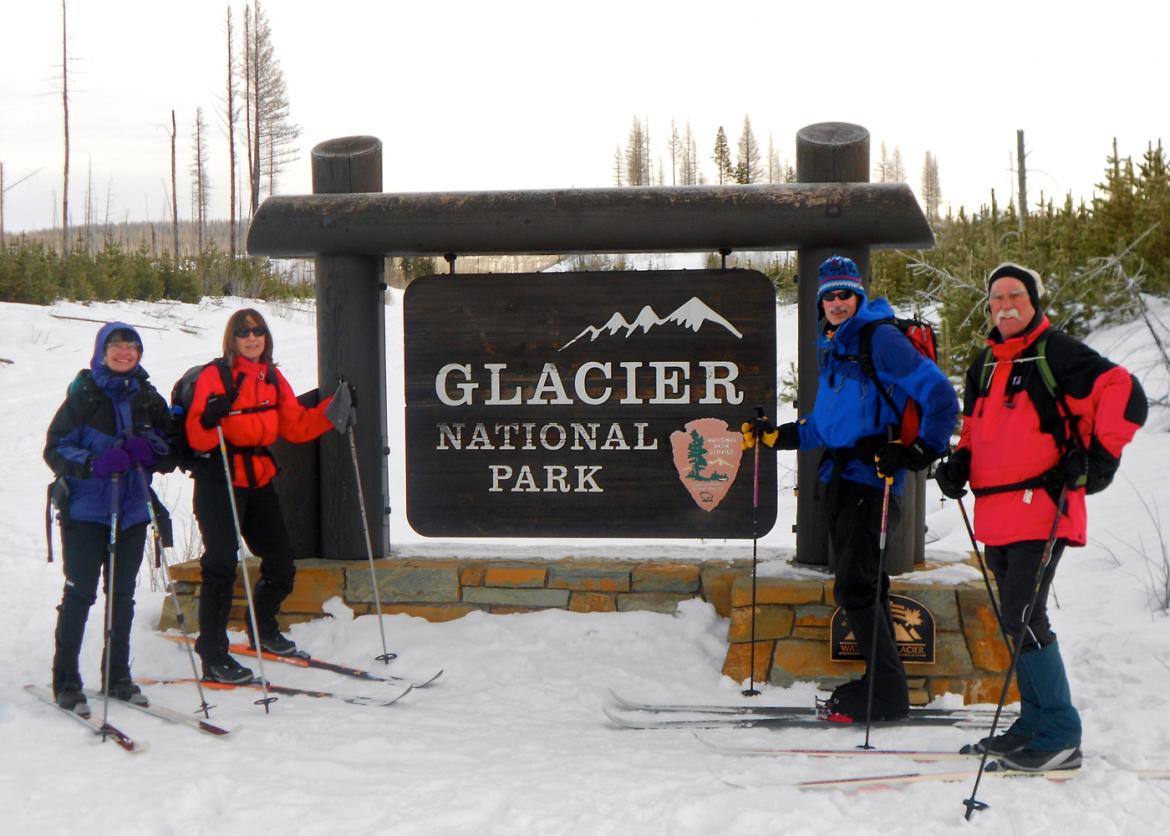 Four skiers pose next to a sign which reads "Glacier national park."