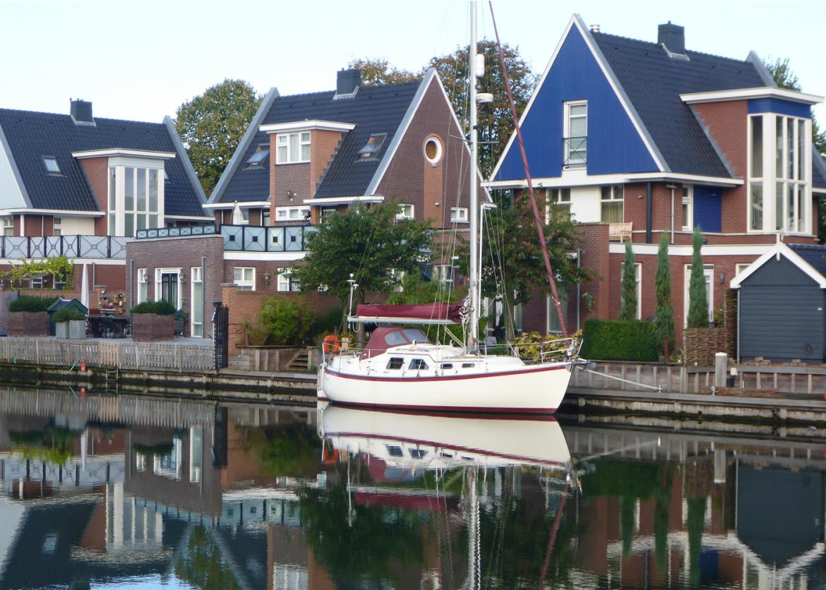 A sailboat docked in the water in front of a row of houses.