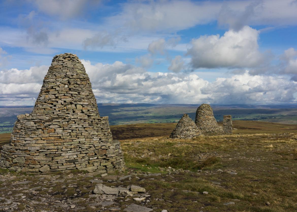 Conical shaped stacked stone structures standing under a partially cloudy sky.