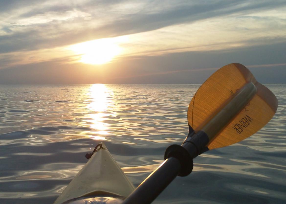 A view from a floating kayak of the sun hanging low in the sky.