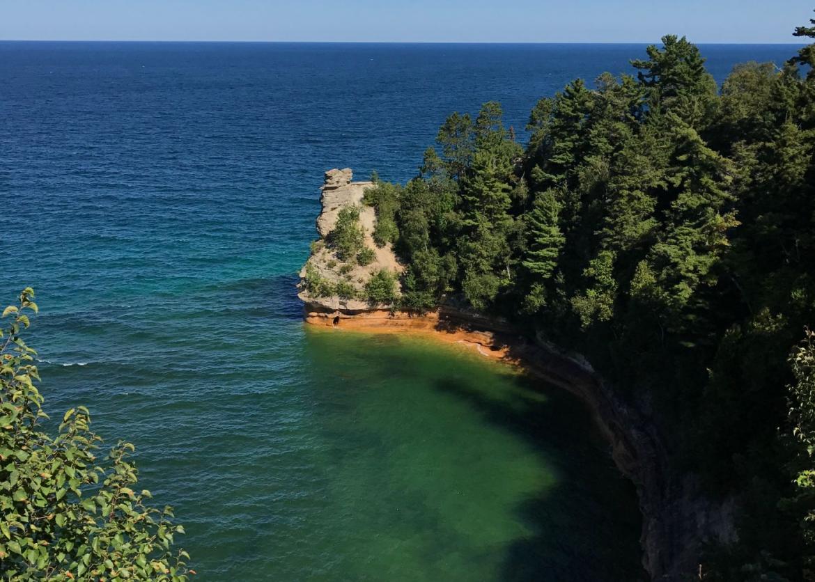 A dead-end cliff covered with trees surrounded by the water.