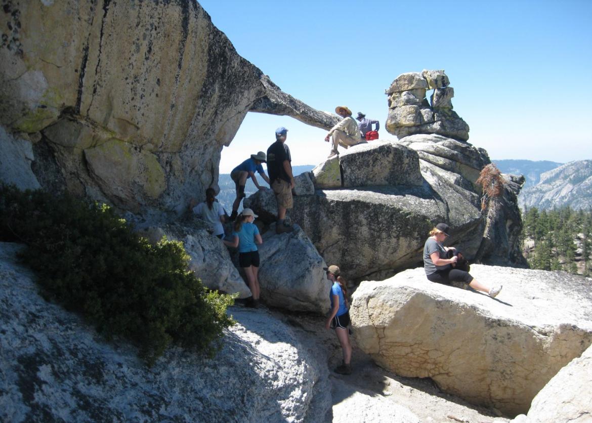 Eight people climb and sit at various points on a rocky outlook.