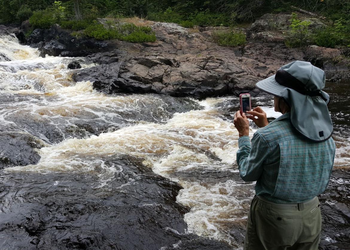 A person standing by the stream, taking a photo of it.