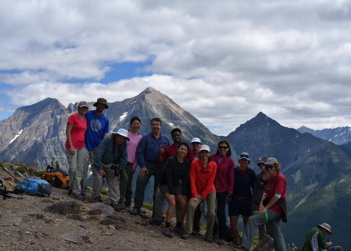 A group photo of thirteen smiling people posing on a moutainside.