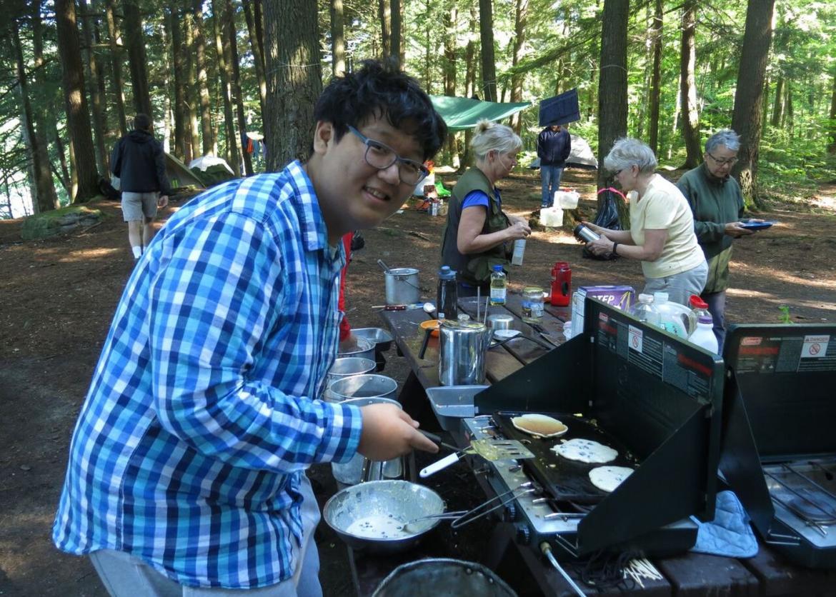 A man in glasses cooking pancakes outdoors.