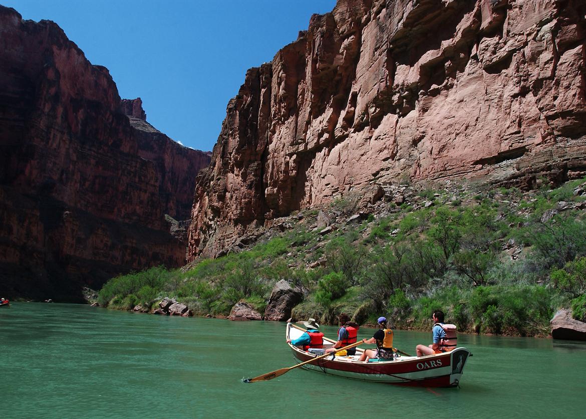 Four people on a rowboat paddling on a river.  The people look up at the walls of the canyon.