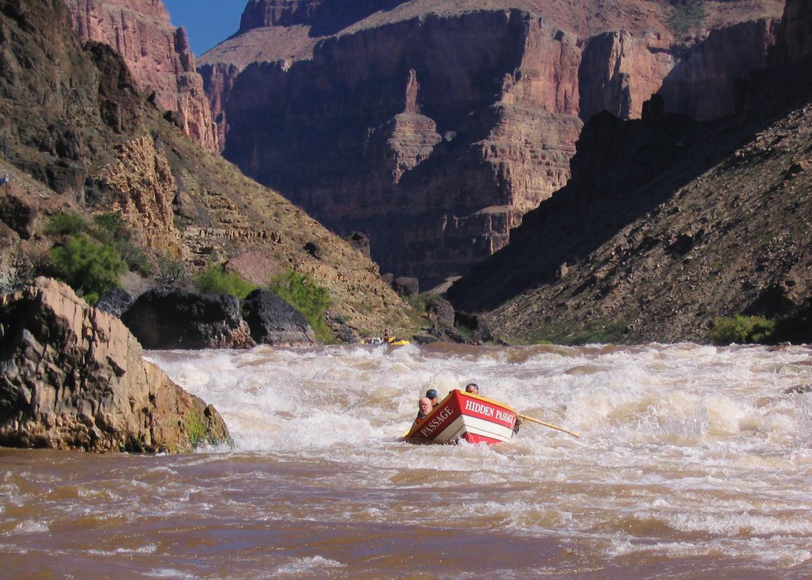 A rowboat paddling through rapids.  The rowboat is labeled "Hidden Passage" on either side of the bow.