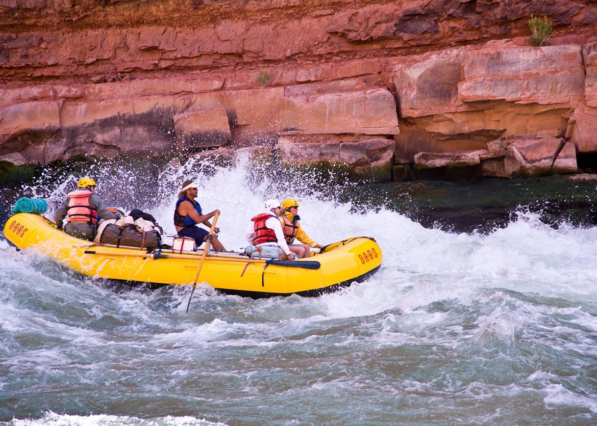 Four people on an inflatable raft going through river rapids.