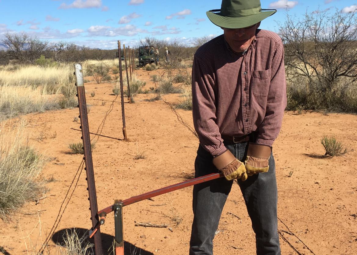 A worker using a tool to fix a barbed wire fence in the desert