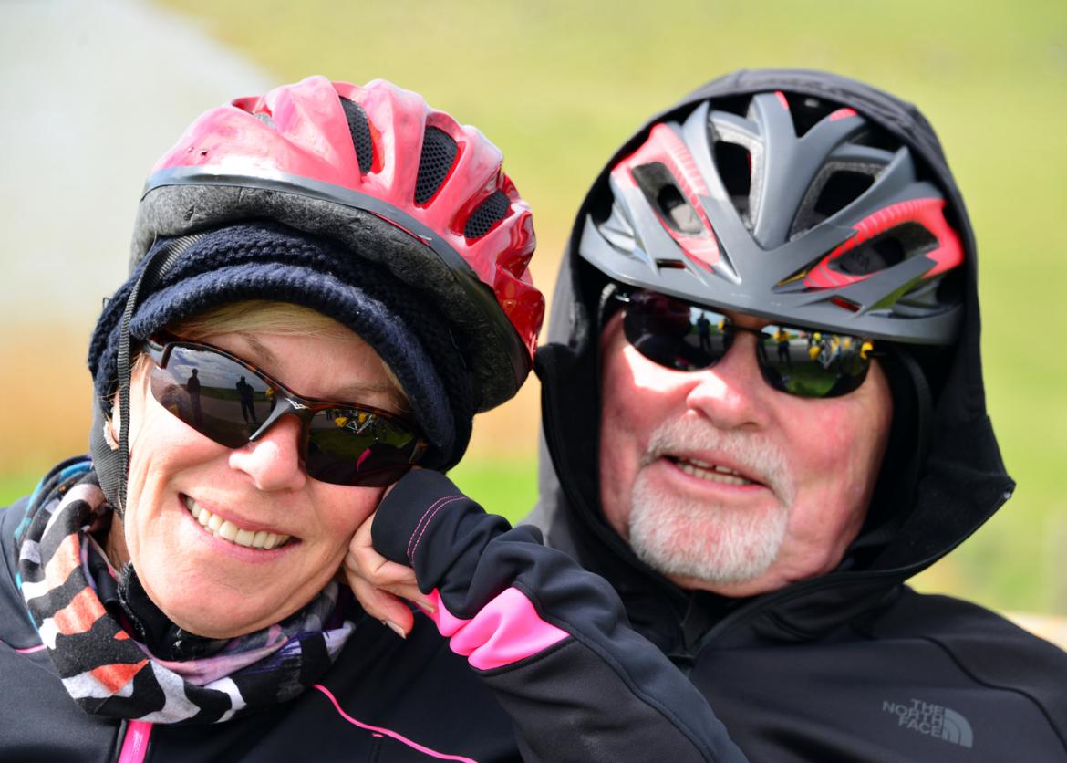 Two people in sunglasses and bike helmets, one smiles for the camera.