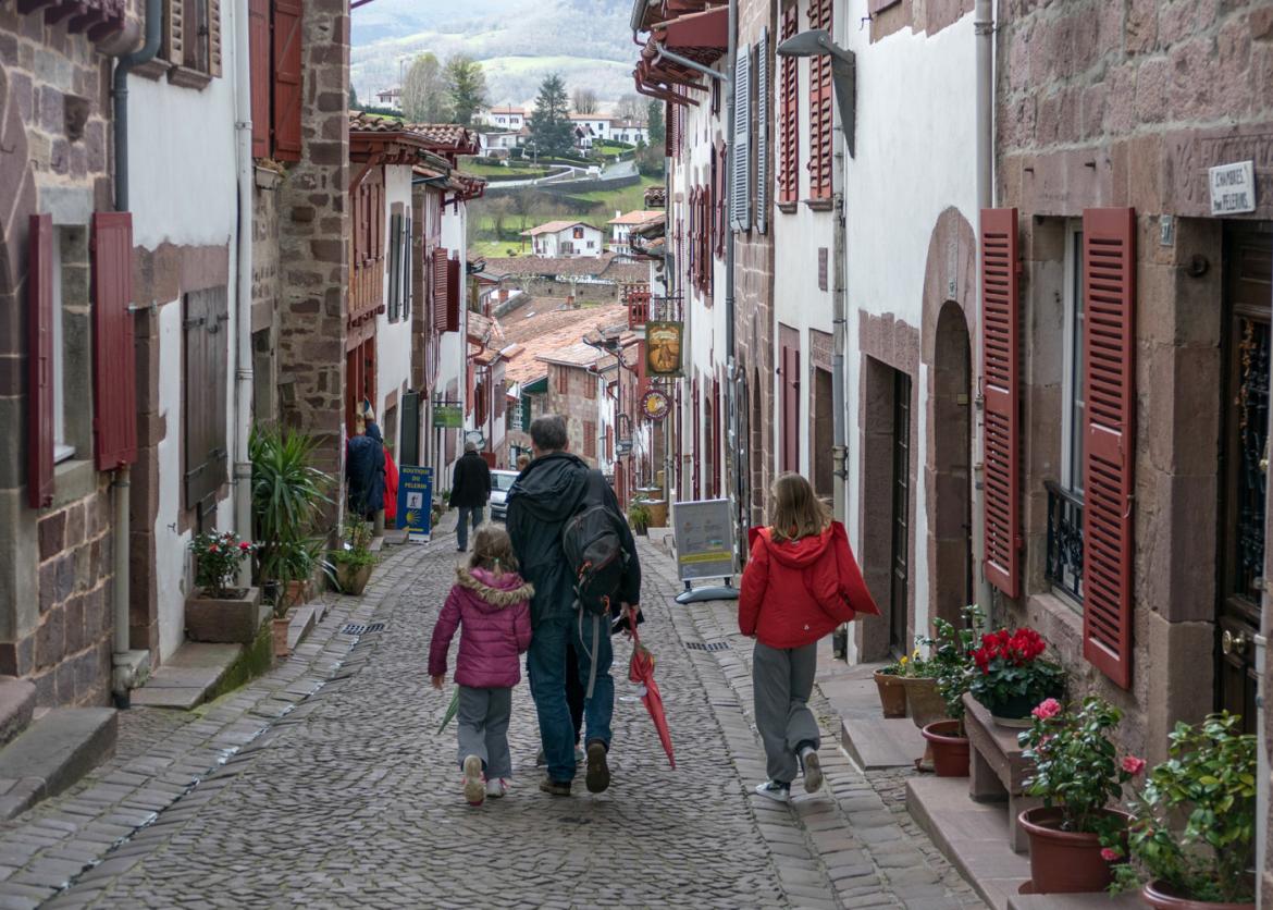An adult walks with two children down a long cobbled street.