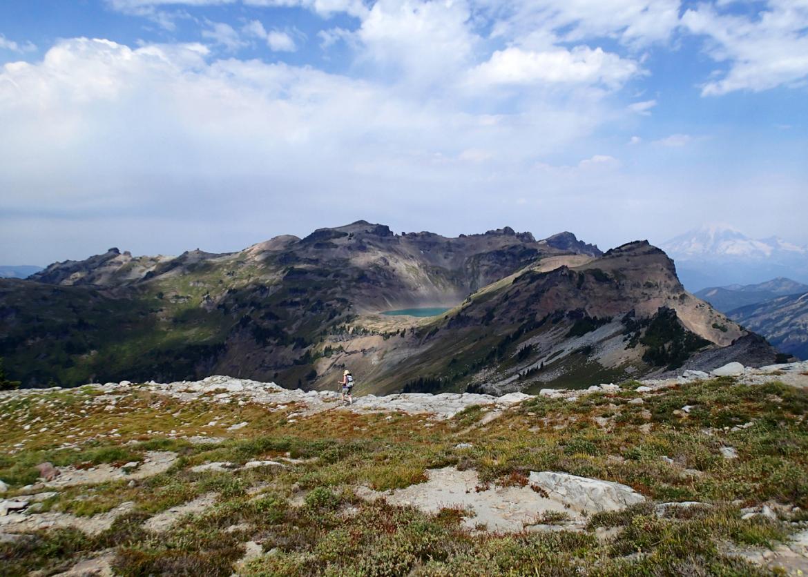 A lone hiker seen against an enormous mountain ridge.