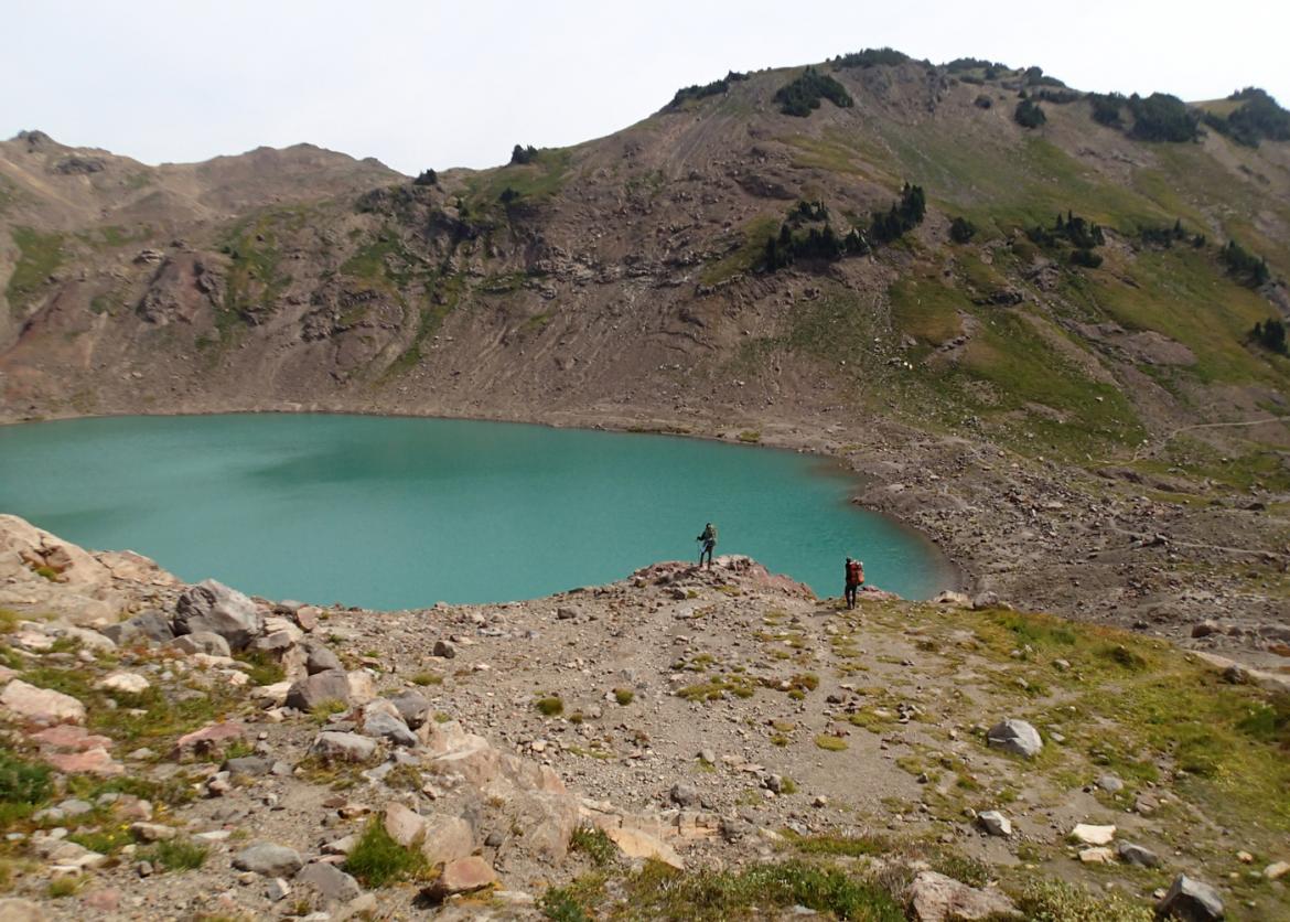 Two hikers on the rim of an alpine lake.