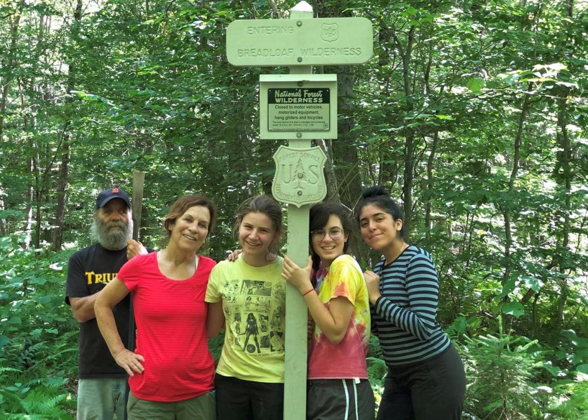 People standing next to a green pole in the woods.
