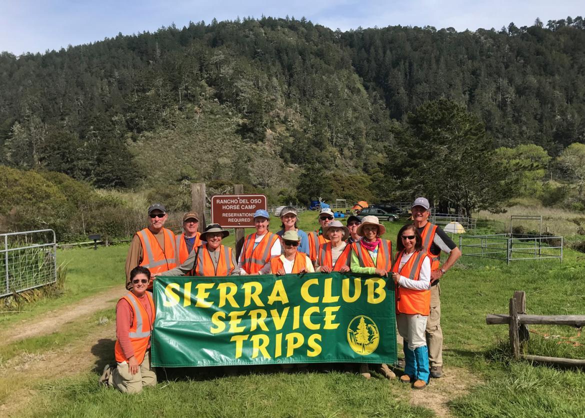A group of people in orange safety vests, holding up a "Sierra Club Service Trips" banner.