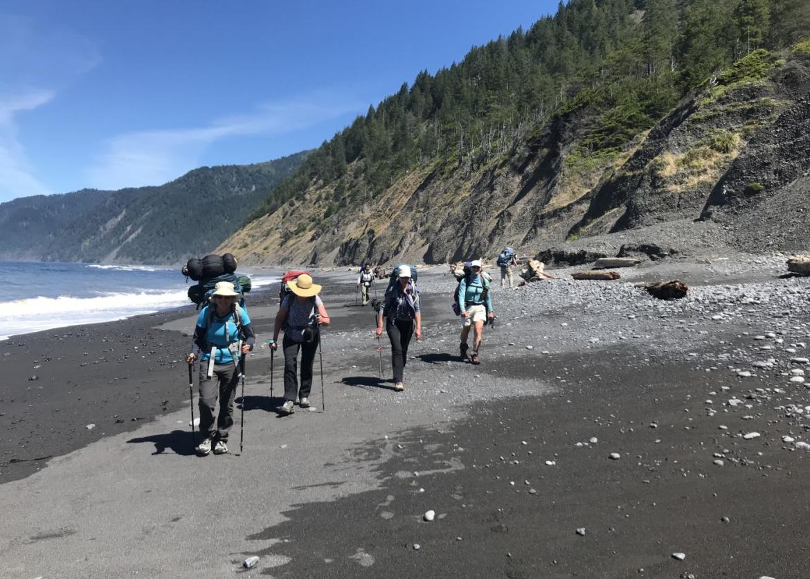 Hikers with trekking poles making their way across the rocky side of the beach.