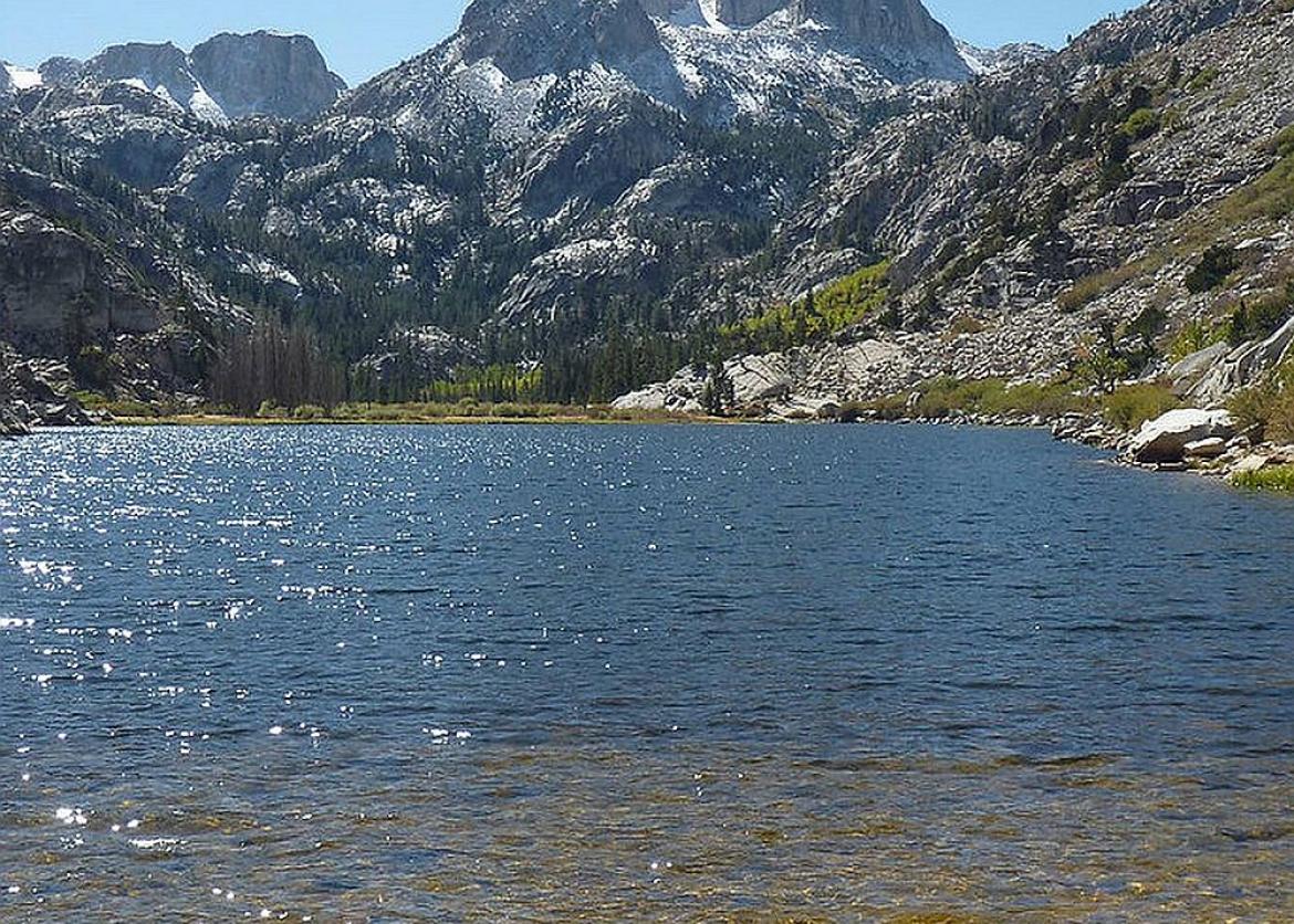 A clear lake glistening with the mountains in the background.