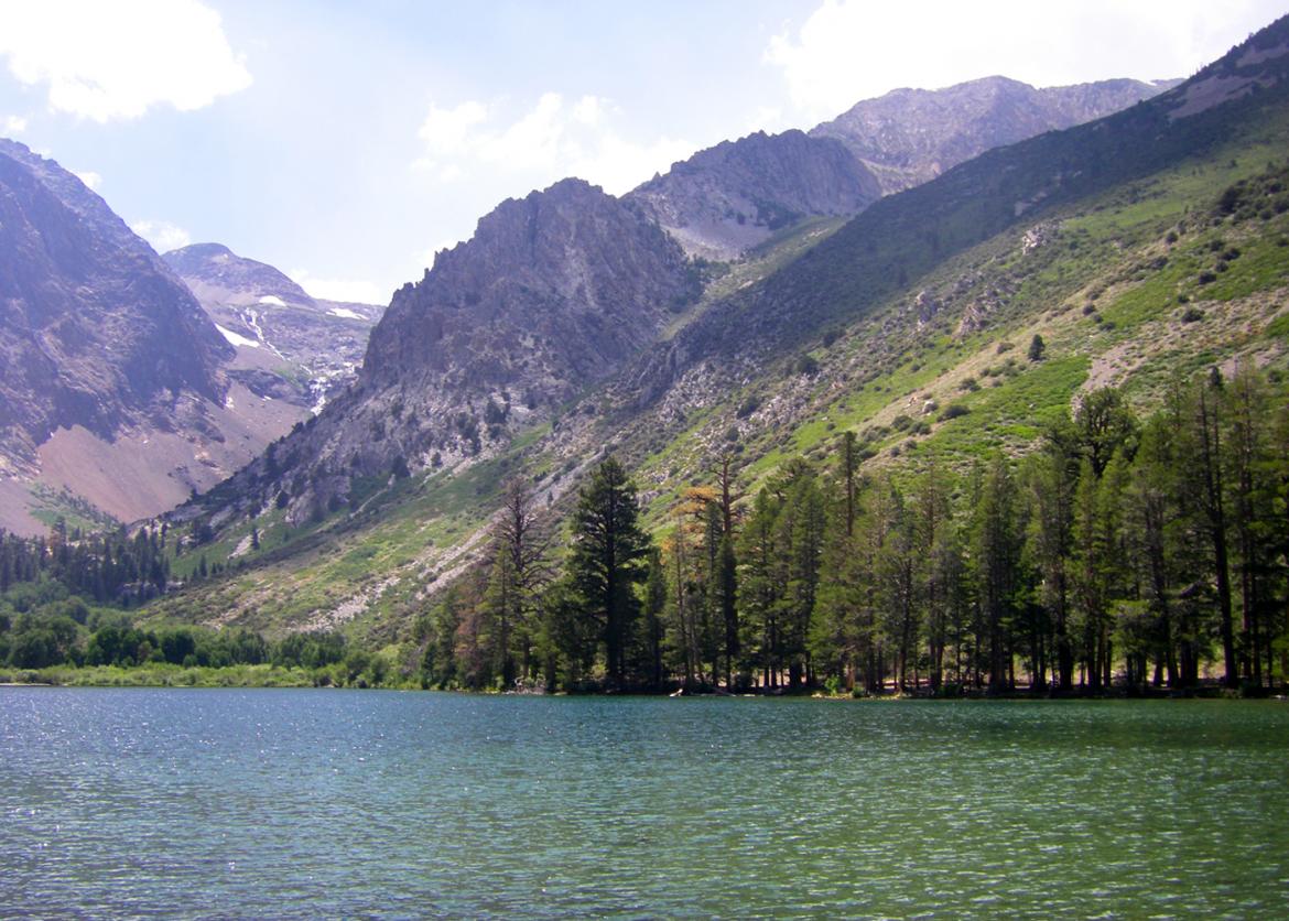A lake at the base of a mountain ridge. The slope is covered with trees and greenery.