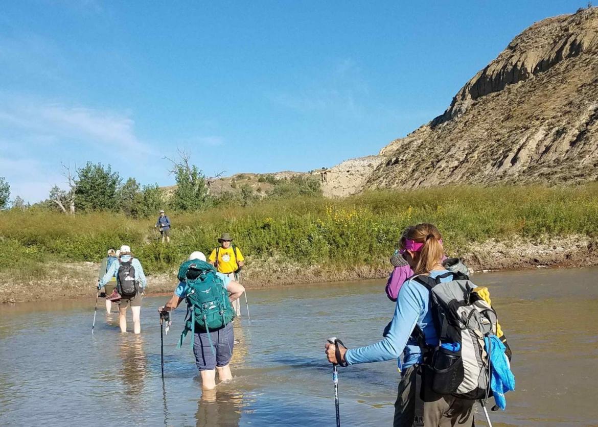 A group of hikers walking across the water with their backpack and equipment on.