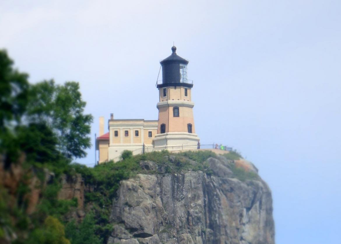 A small, beige building with a lighthouse next to it on a cliff.