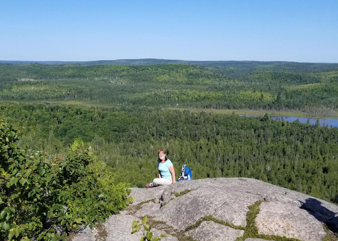 A women sitting on the cliff with a blue backpack next to her.